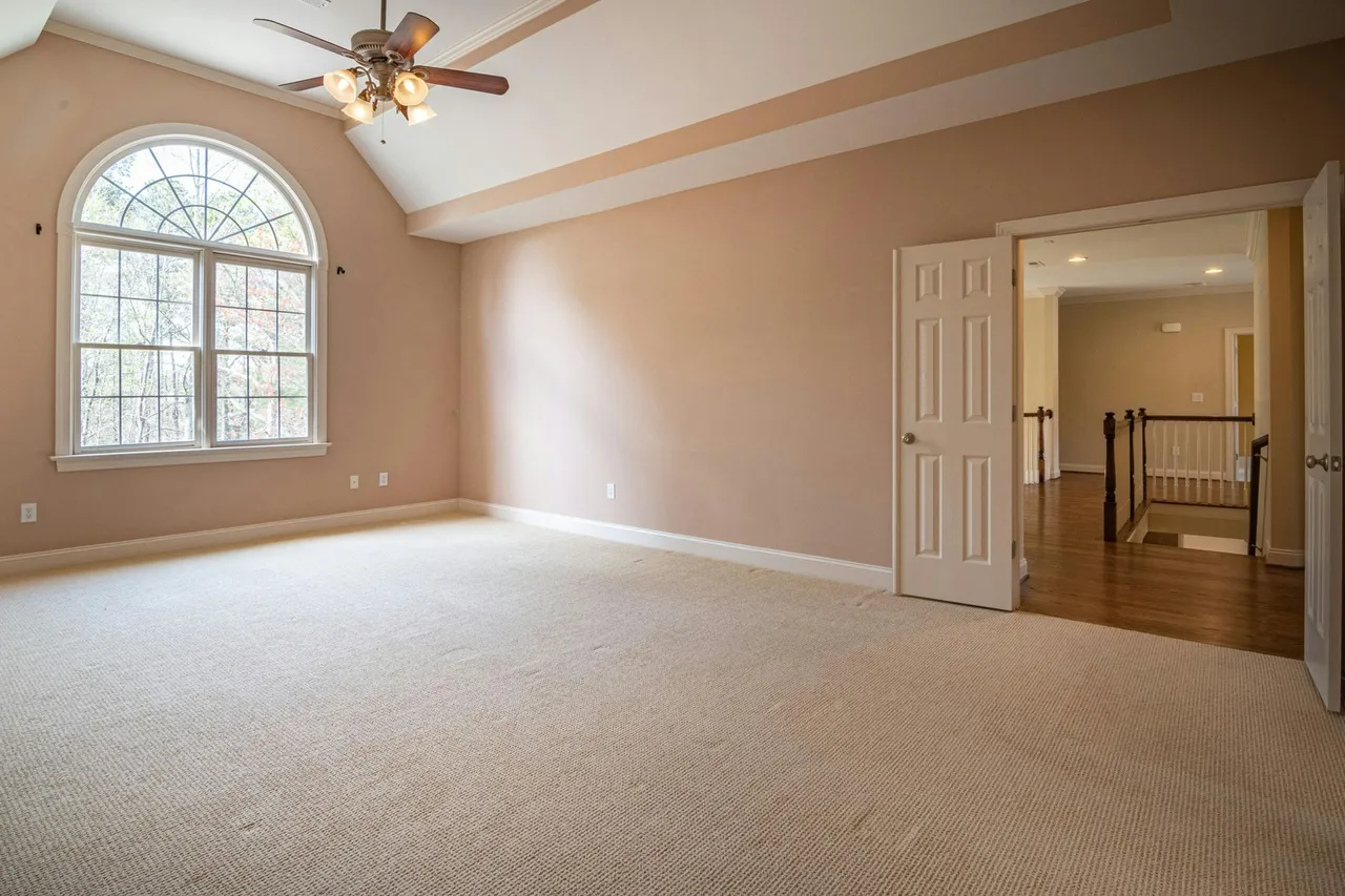 A modern living room with hardwood floors, a dark sofa, a coffee table, and large windows overlooking autumn trees.