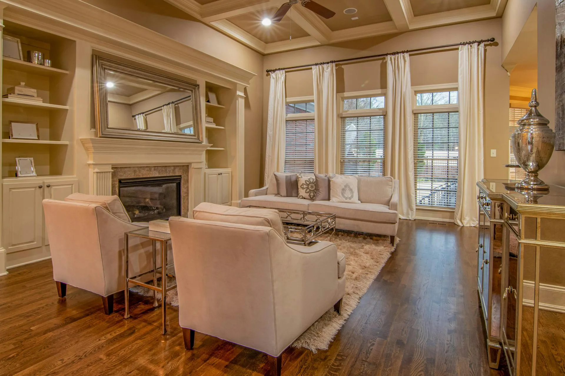 A modern living room with hardwood floors, a dark sofa, a coffee table, and large windows overlooking autumn trees.