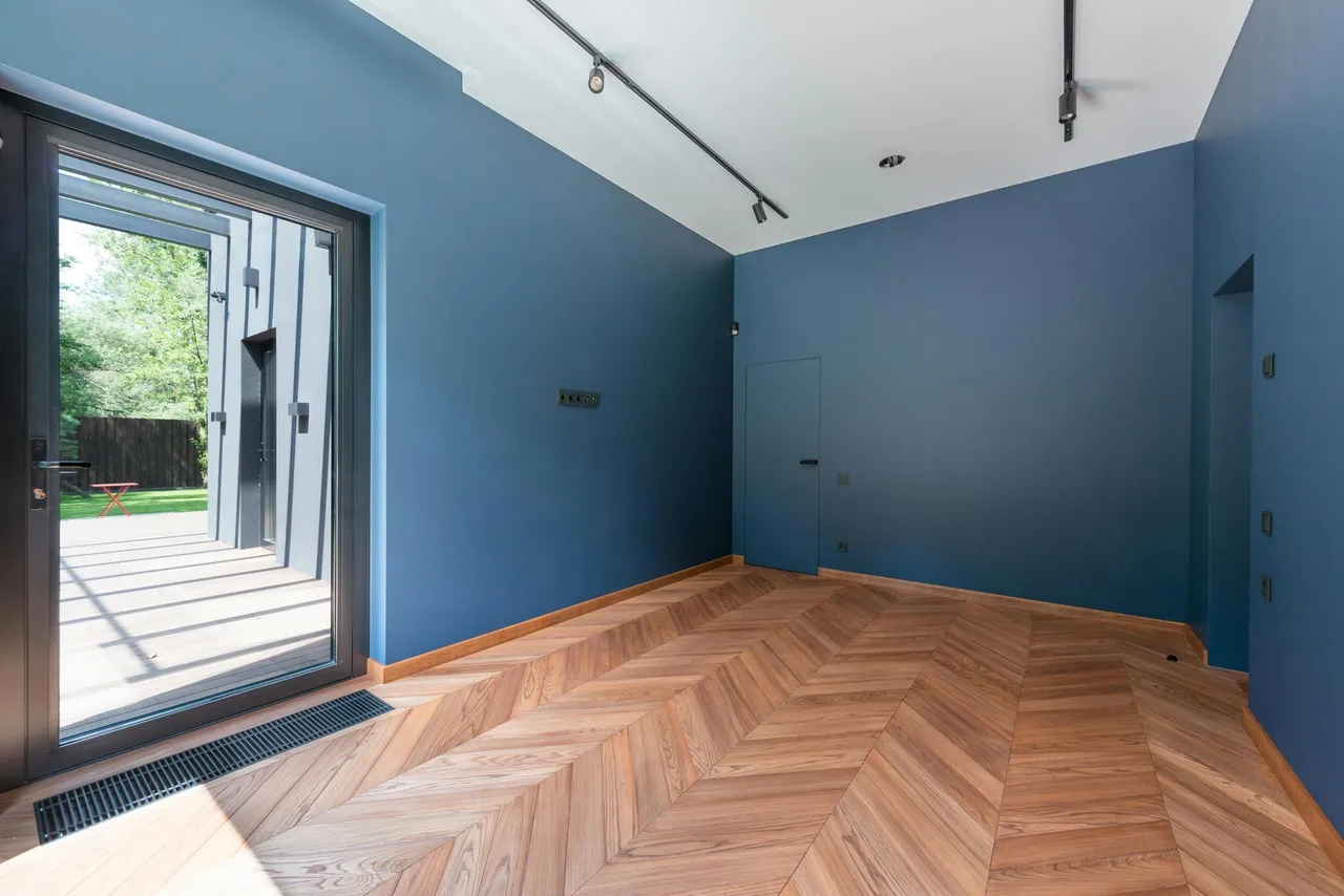 Empty blue room with herringbone wood floor and open glass doors to a patio