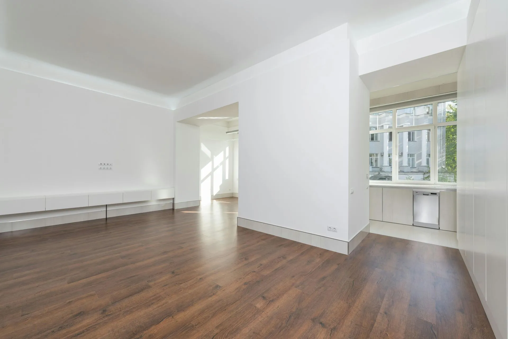 Empty white living room with wood floors, a built-in bench, and large windows letting in daylight