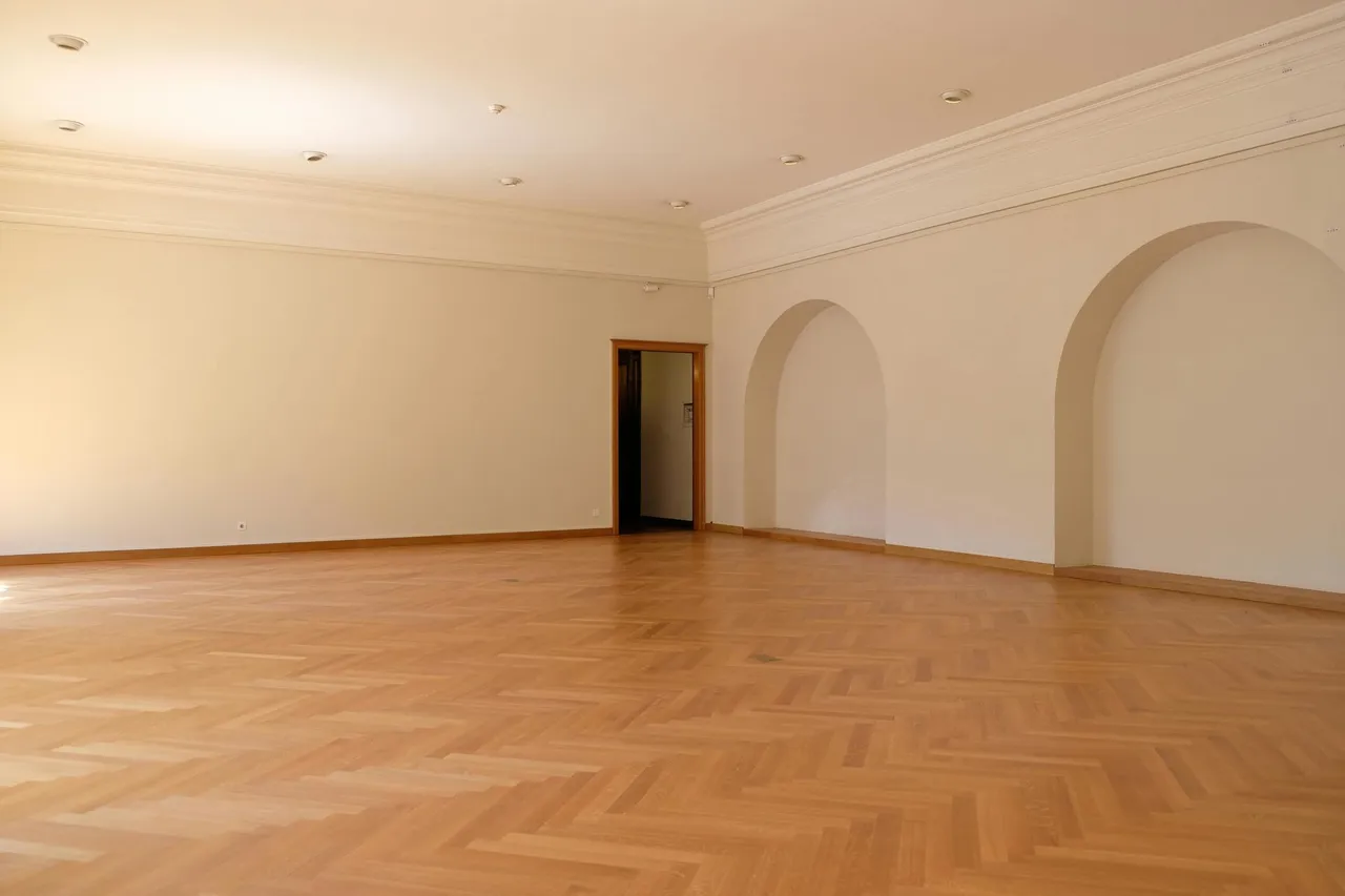 A modern living room with hardwood floors, a dark sofa, a coffee table, and large windows overlooking autumn trees.