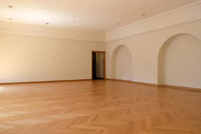 A modern living room with hardwood floors, a dark sofa, a coffee table, and large windows overlooking autumn trees.