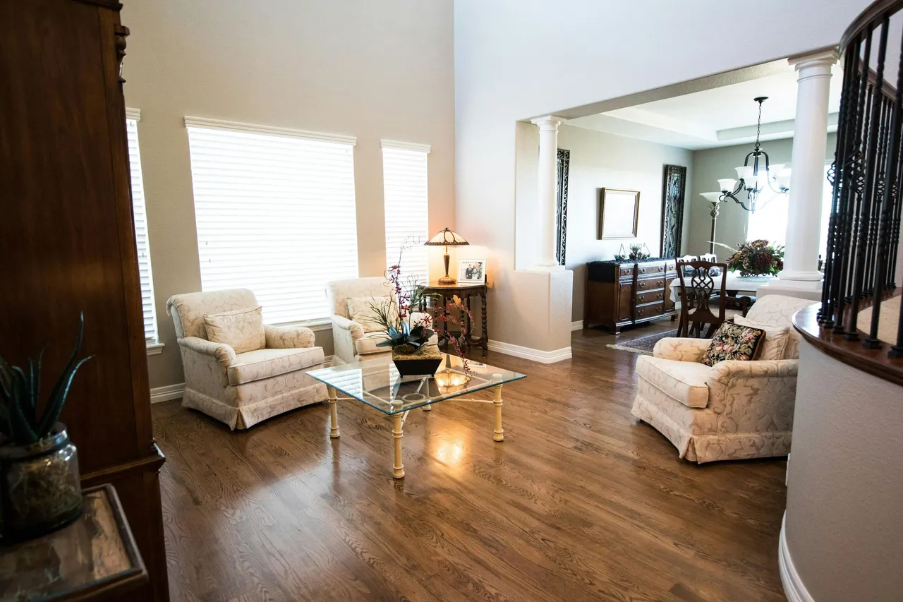 A modern living room with hardwood floors, a dark sofa, a coffee table, and large windows overlooking autumn trees.