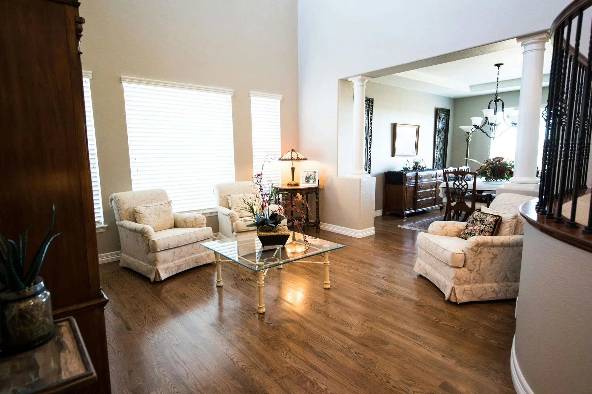 A modern living room with hardwood floors, a dark sofa, a coffee table, and large windows overlooking autumn trees.