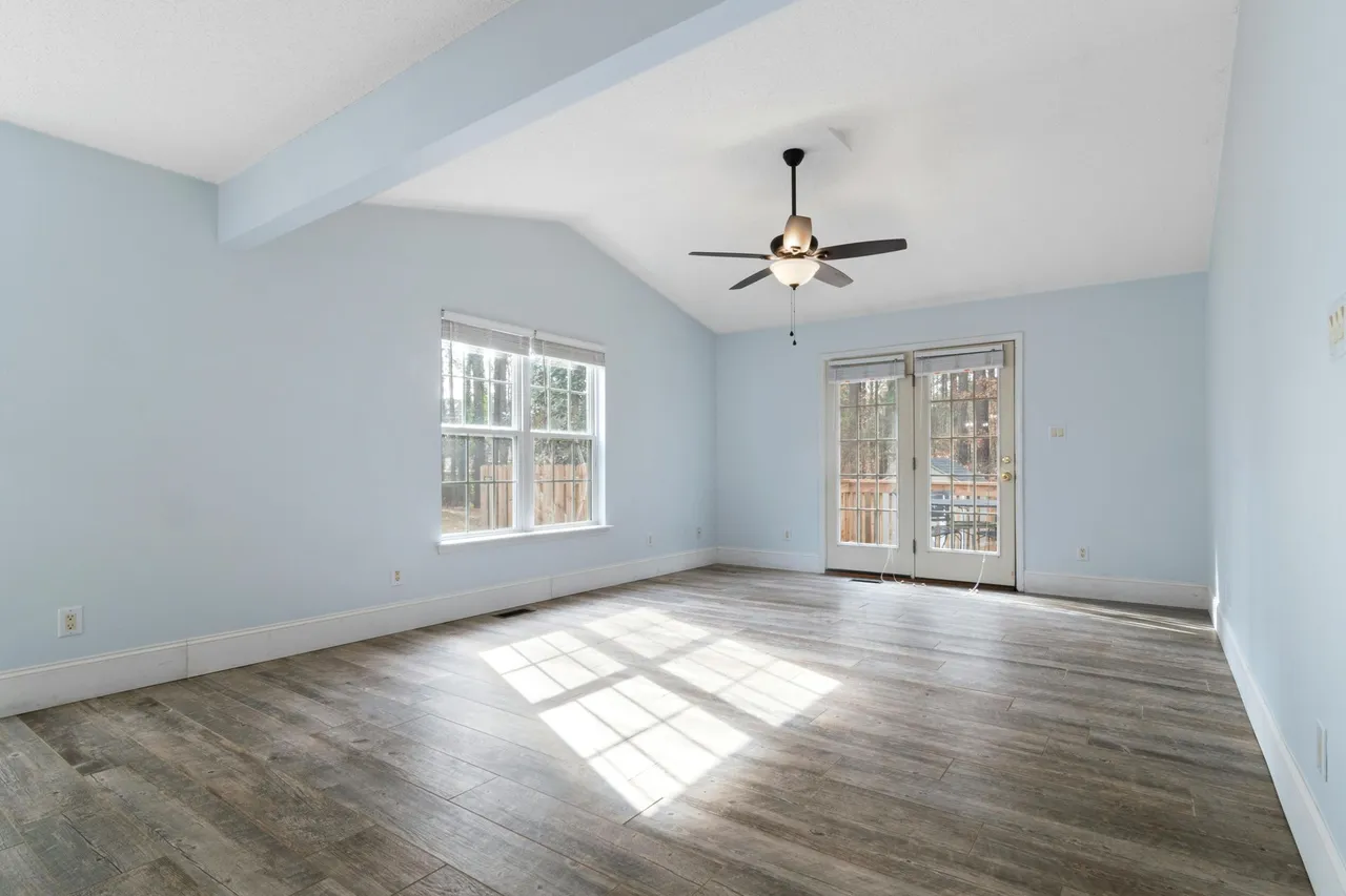 A modern living room with hardwood floors, a dark sofa, a coffee table, and large windows overlooking autumn trees.