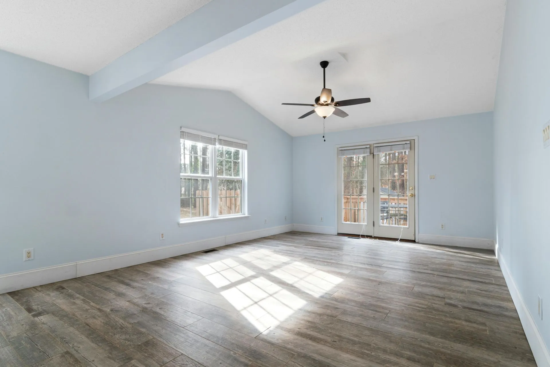 A modern living room with hardwood floors, a dark sofa, a coffee table, and large windows overlooking autumn trees.