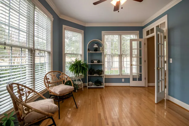 Bright sunroom with wicker chairs, blue walls, tall windows, plants, and a wood floor.