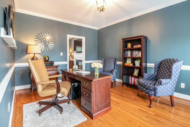 A modern living room with hardwood floors, a dark sofa, a coffee table, and large windows overlooking autumn trees.