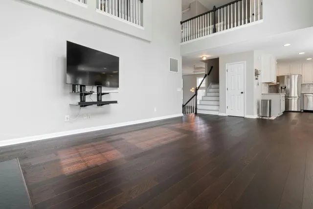 A modern living room with hardwood floors, a dark sofa, a coffee table, and large windows overlooking autumn trees.