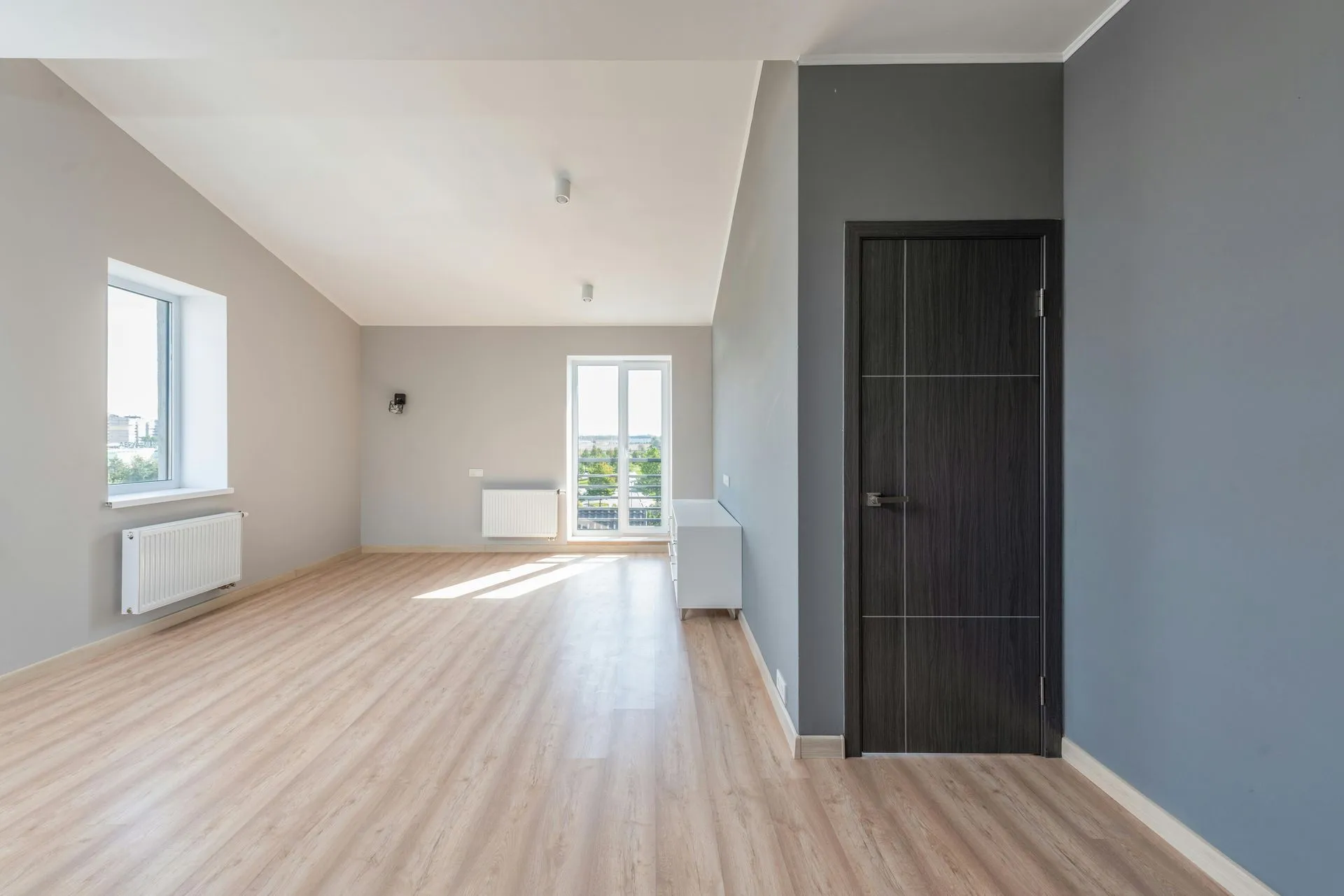 A modern living room with hardwood floors, a dark sofa, a coffee table, and large windows overlooking autumn trees.