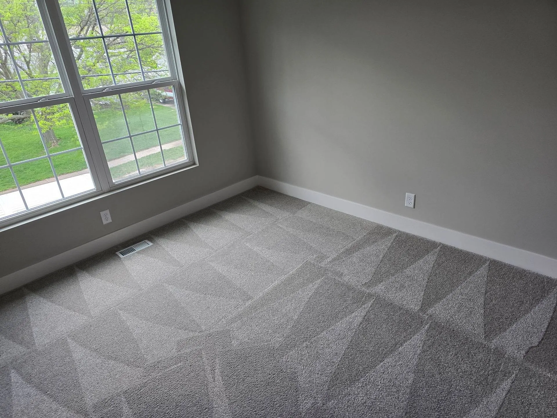 Empty gray-carpeted room with large window and light gray walls