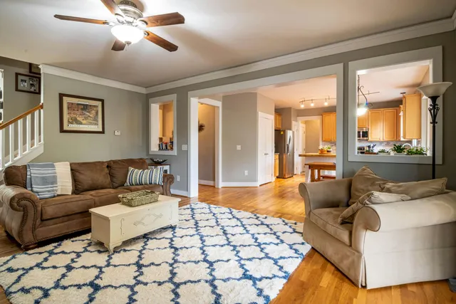 A modern living room with hardwood floors, a dark sofa, a coffee table, and large windows overlooking autumn trees.