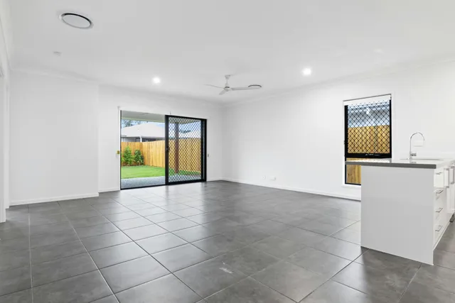 Empty modern living room with gray tile floor, white walls, sliding glass doors, and a small kitchen island.